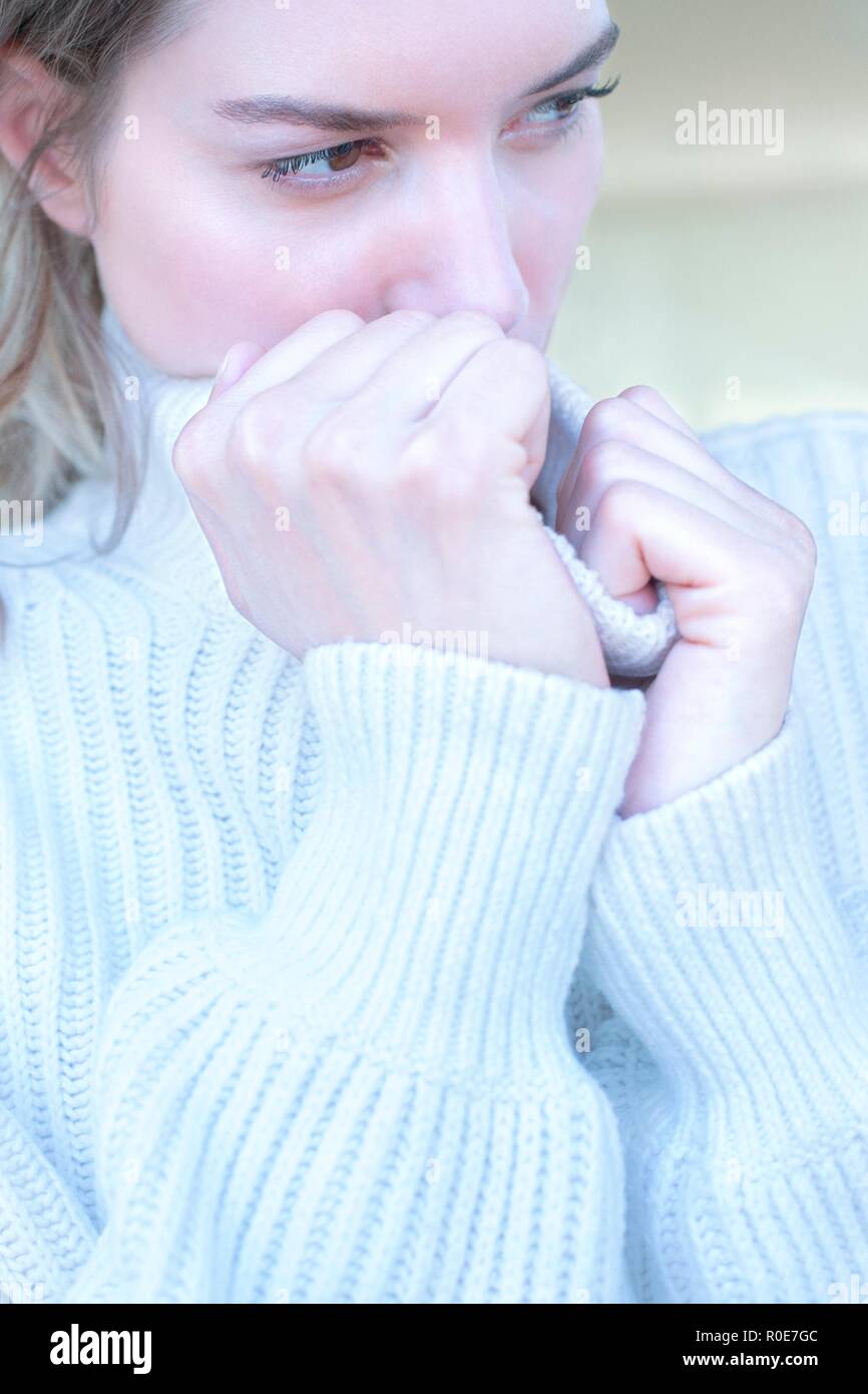 Young woman clasping neck of sweater and looking away with sad expression. Stock Photo