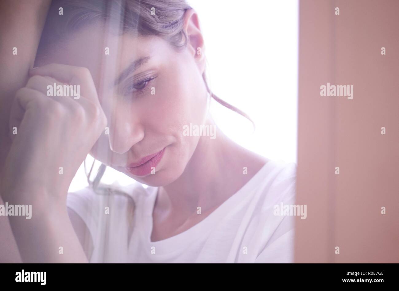 Young woman with eyes closed clasping hands against window. Stock Photo
