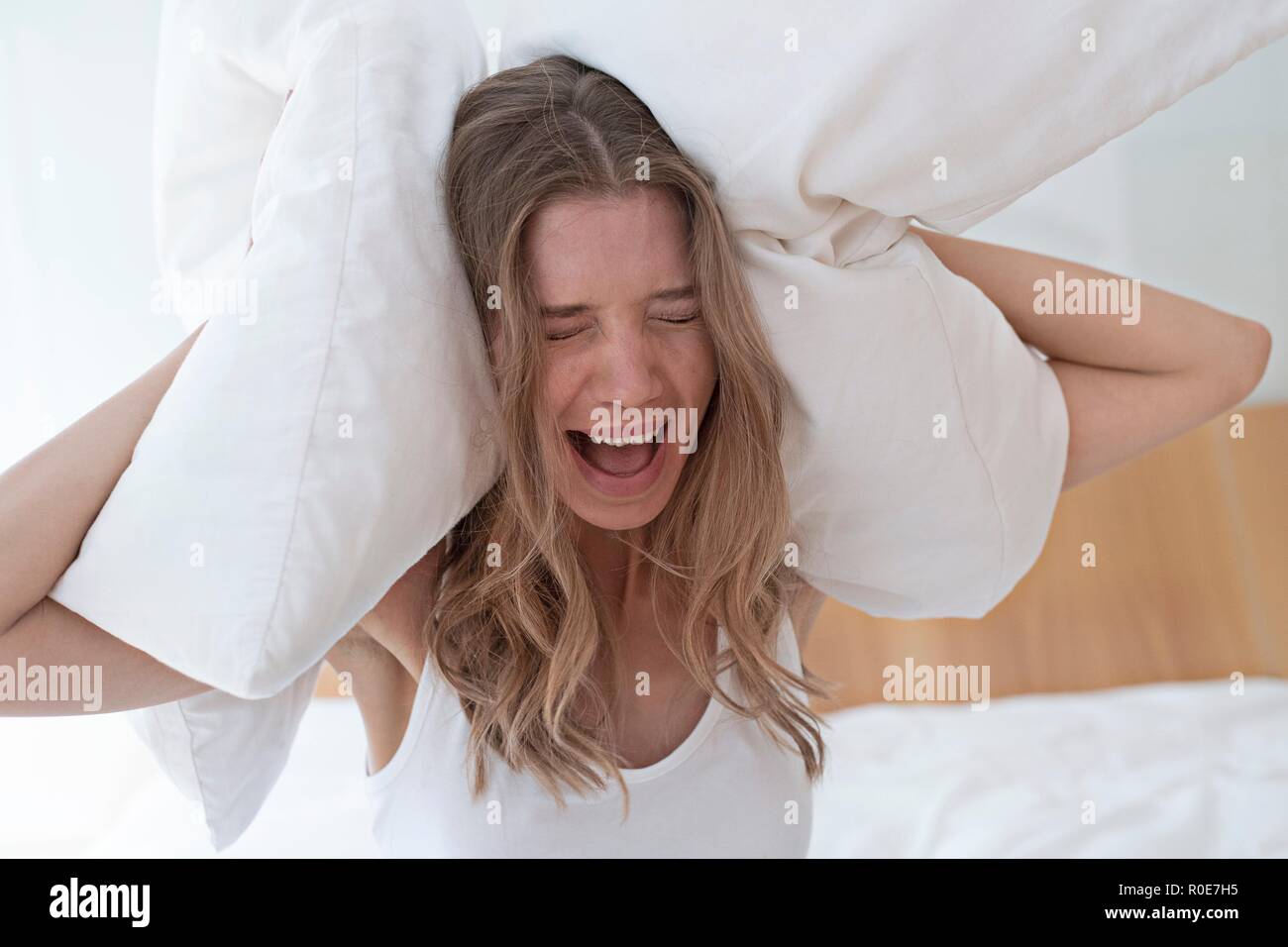 Young woman holding pillow over her ears and screaming. Stock Photo
