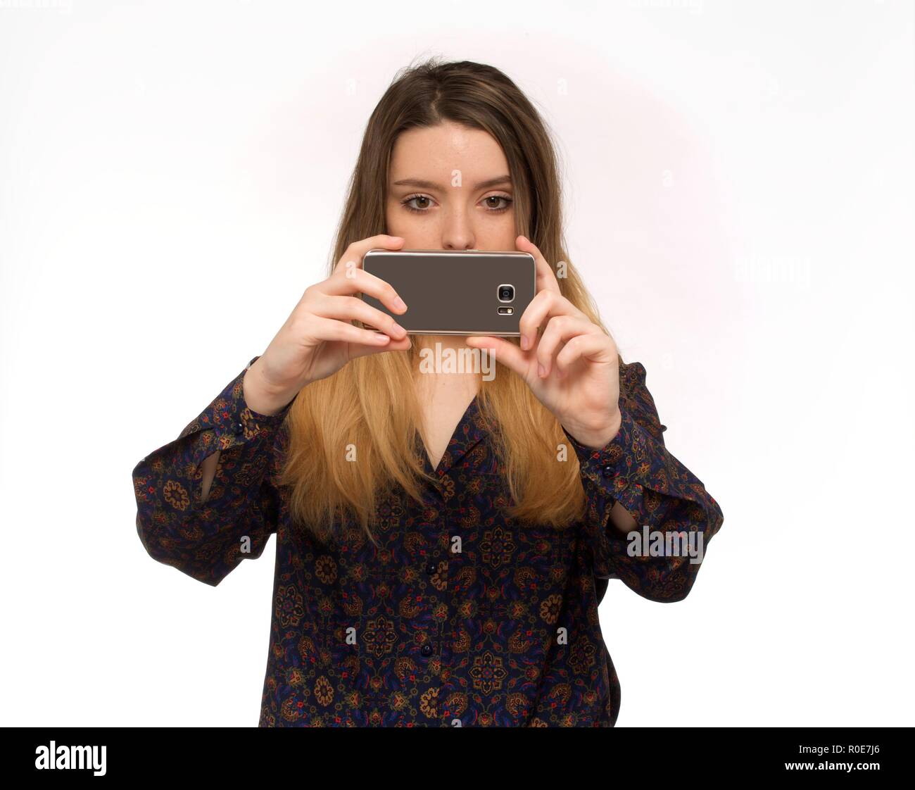 Young woman taking photo with smartphone against white background. Stock Photo