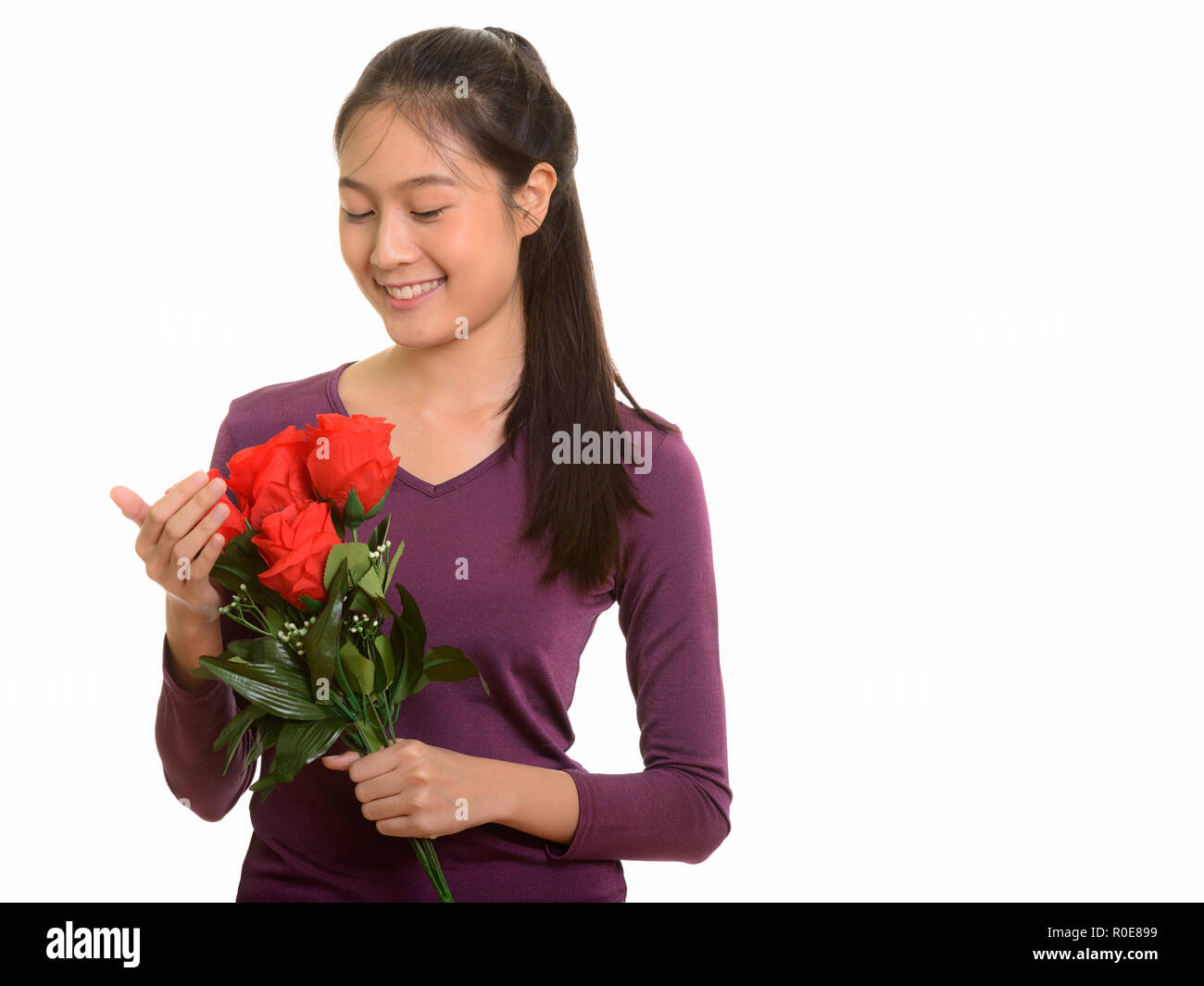 Young happy Asian teenage girl smiling holding red roses ready f Stock Photo