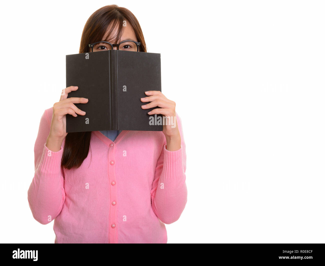 Young Asian teenage girl hiding behind book Stock Photo