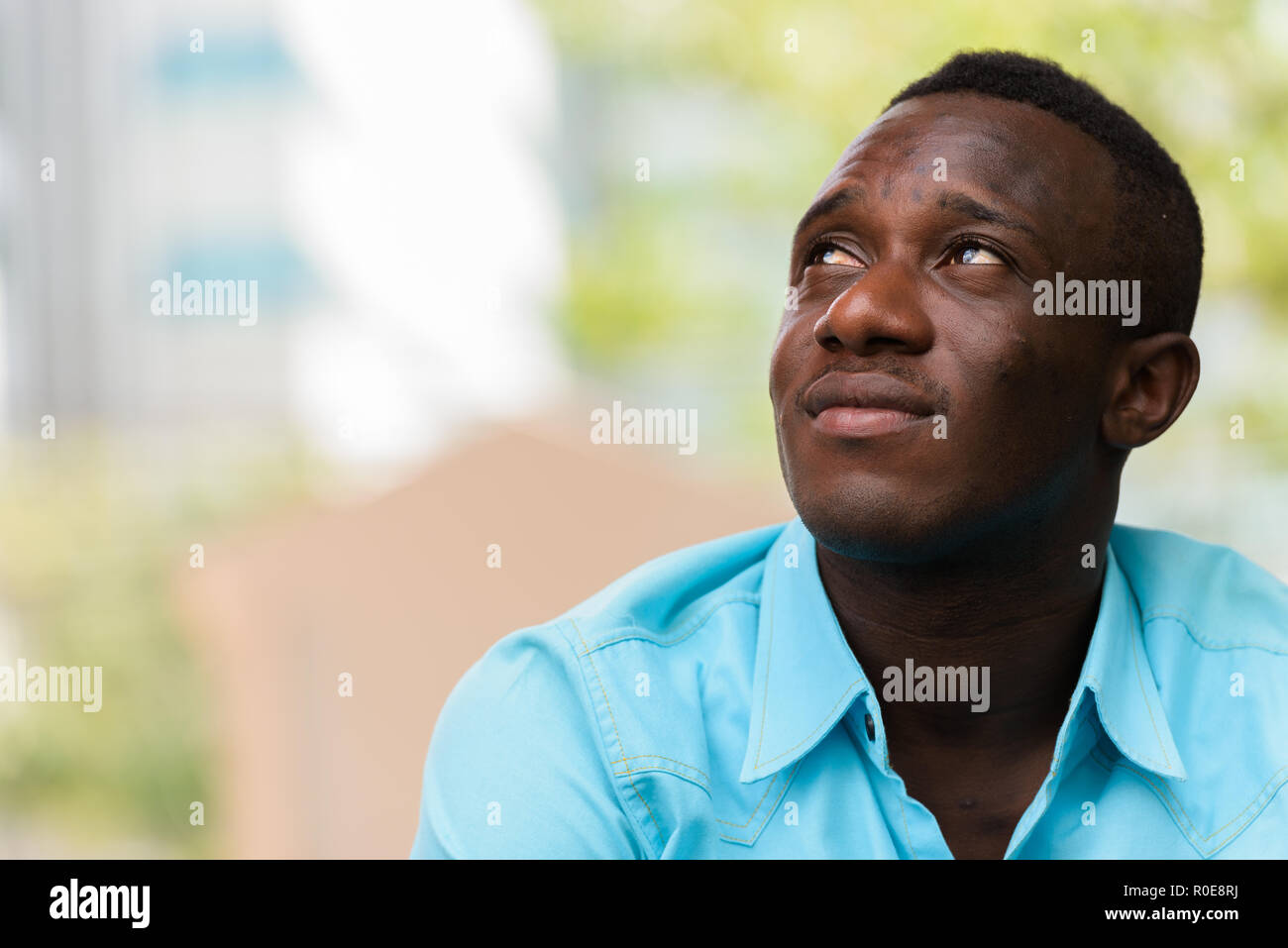 Young black African man sitting while thinking and looking up ou Stock Photo