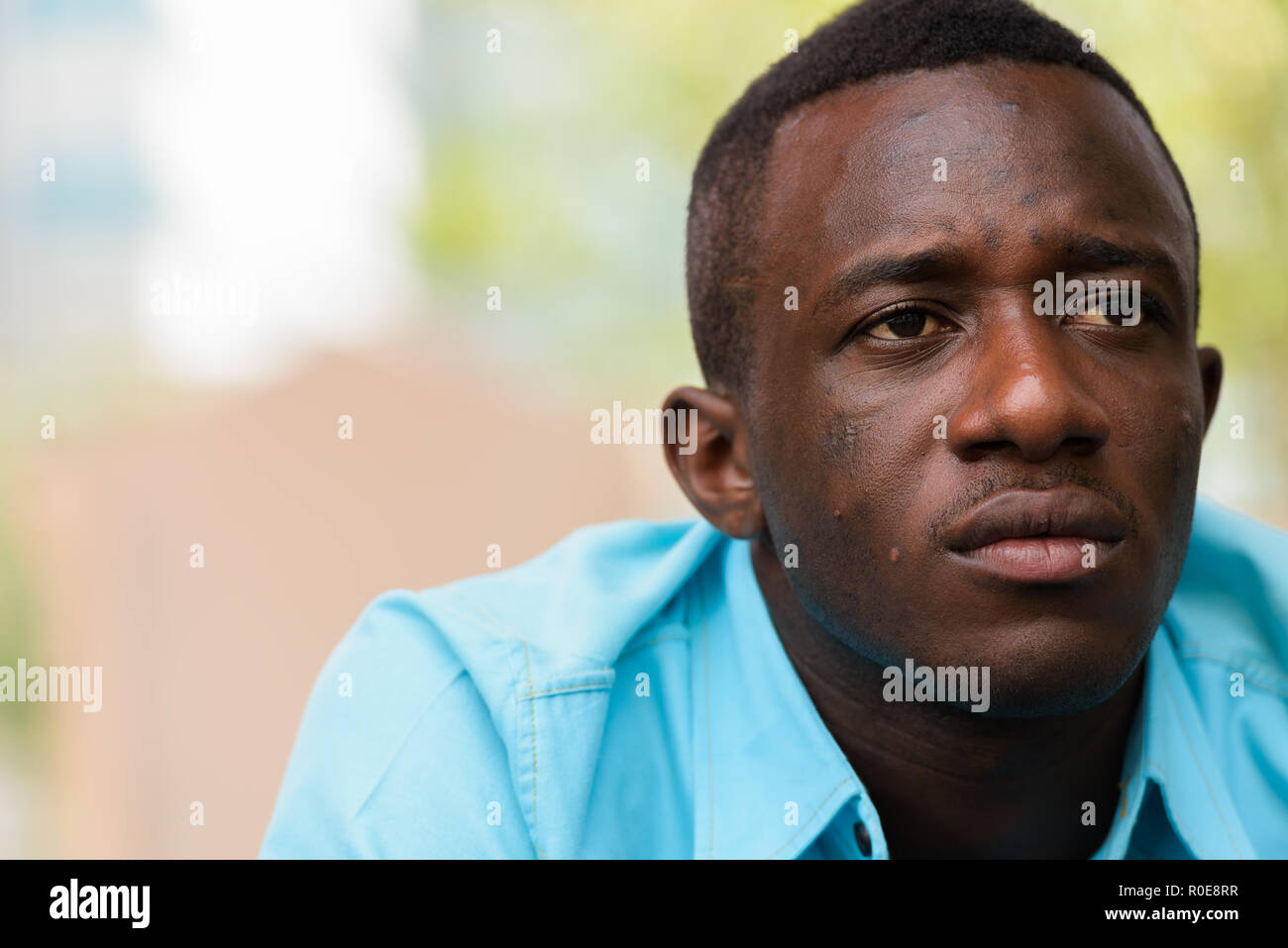 Close up of young black African man sitting while thinking outsi Stock Photo