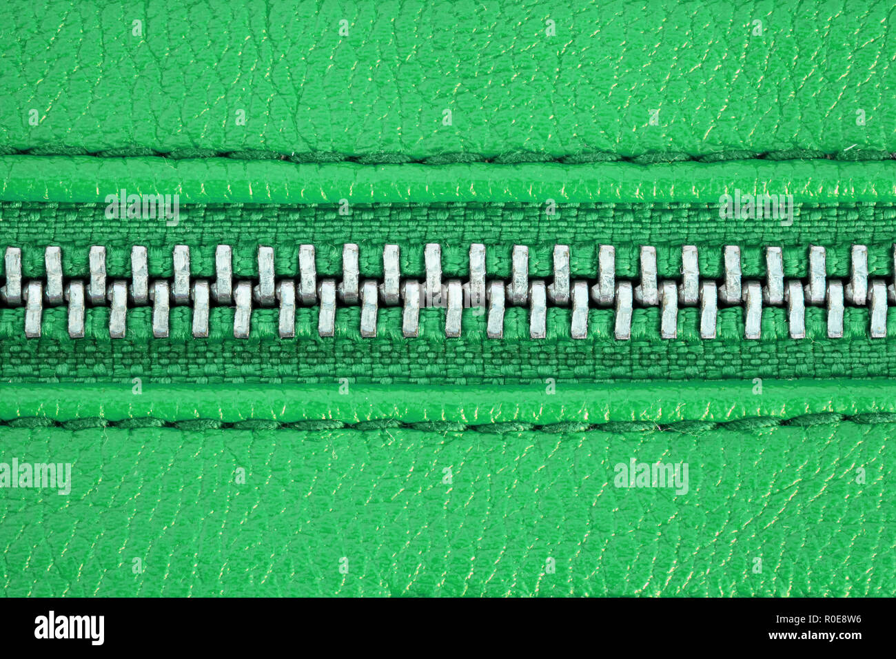 Zipper tightly closed binding together two layers of green fabric textile and green leather under high magnification close detail photography as fashi Stock Photo