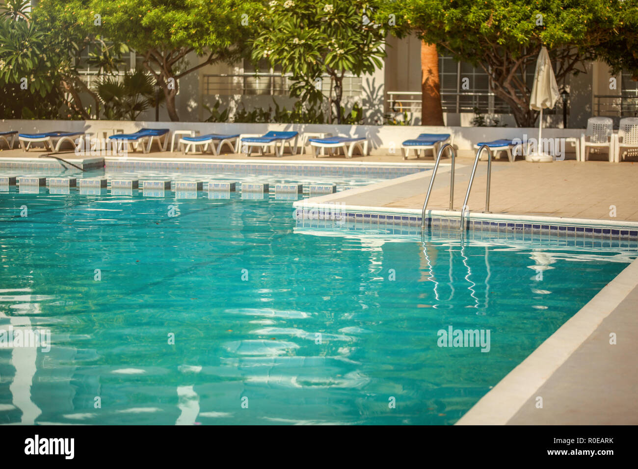 Empty hotel resort swimming pool, lit by morning sun, few leaves on the water surface Stock Photo