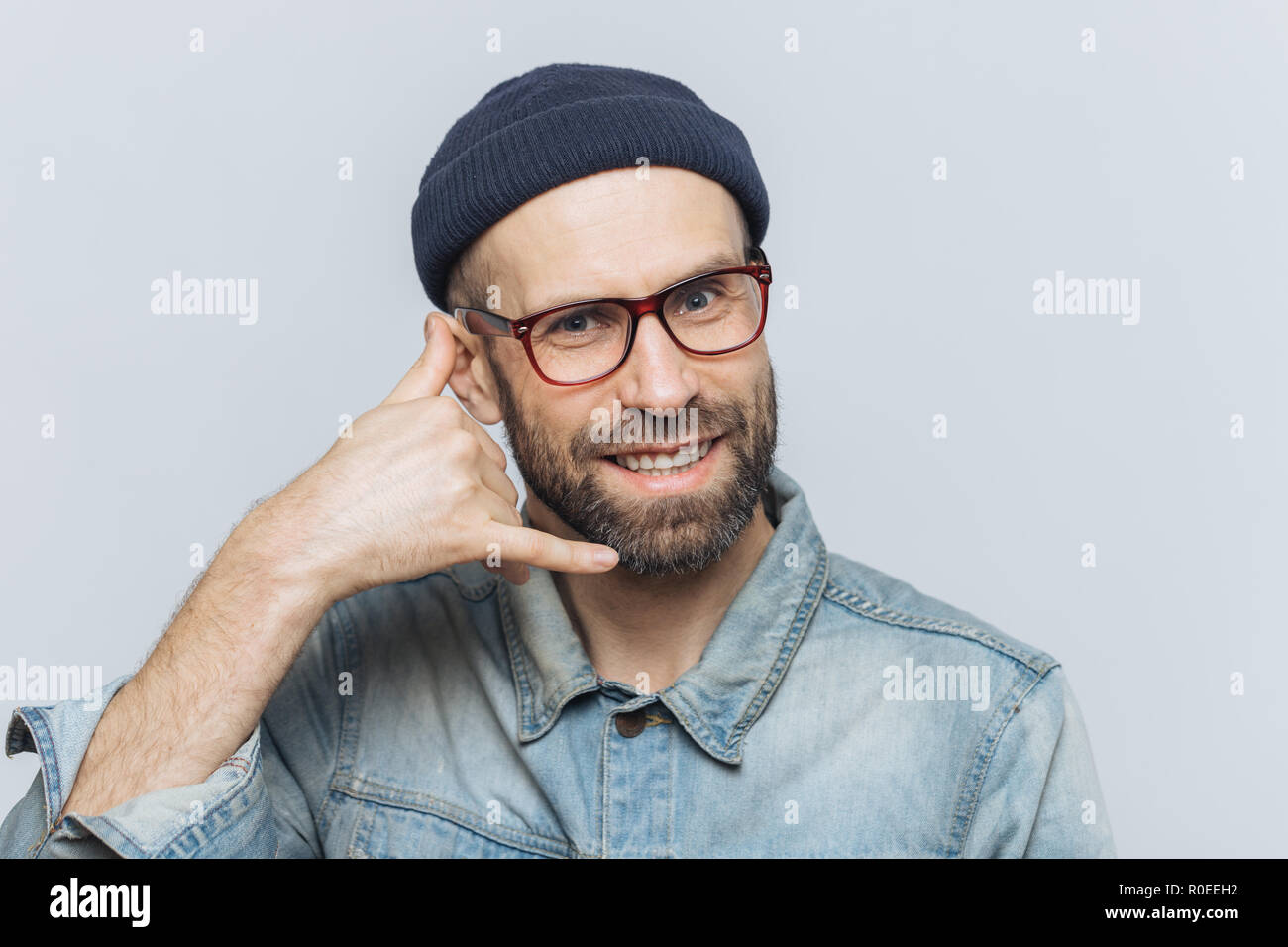 Call me please! Happy handsome man holds hand near ear, imitates mobile phone conversation, smiles joyfully, waits for call from someone, isolated ove Stock Photo