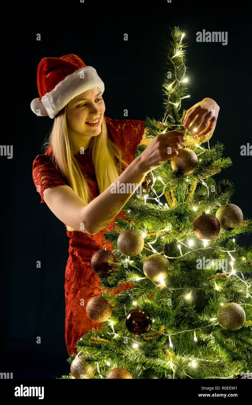 Young woman decorates the Christmas tree. Elf and spruce with decorations. Girl and adornment. Stock Photo