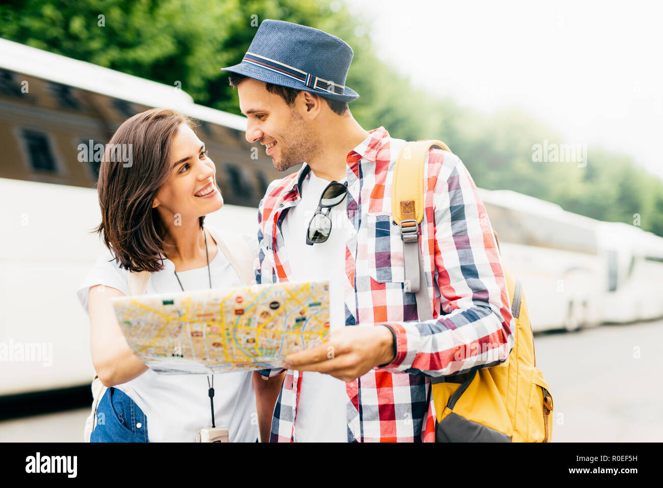 Attractive male and female tourists, being in unfamiliar place, holding map or city guide, deciding where to go first, looking happily at each other,  Stock Photo