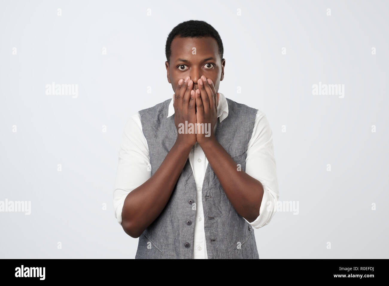 African american young man in white shirt and vest with hand over his mouth, stunned and speechless Stock Photo