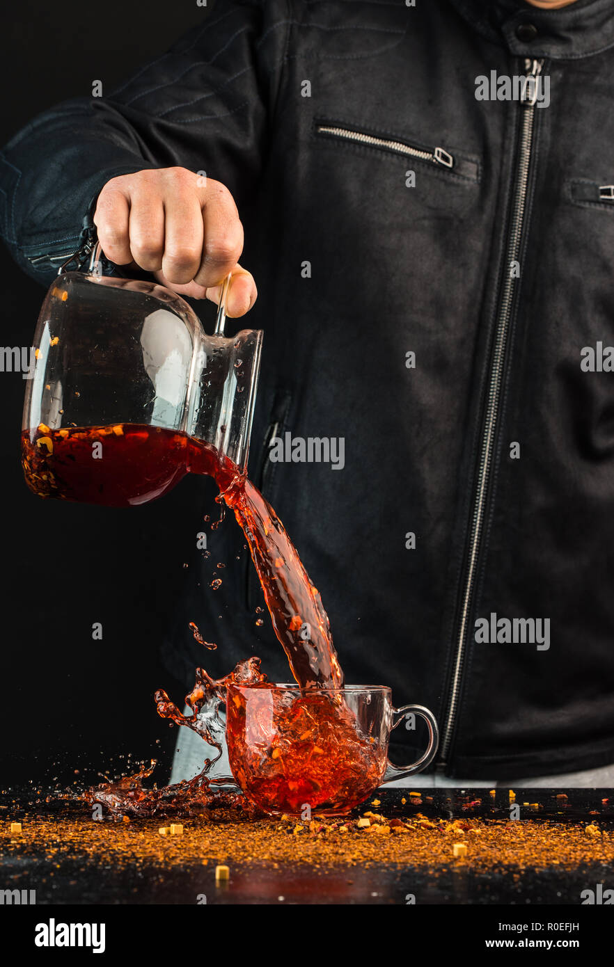 a man pours a drink from a jug into a glass cup, you can see drops and a liquid splash Stock Photo