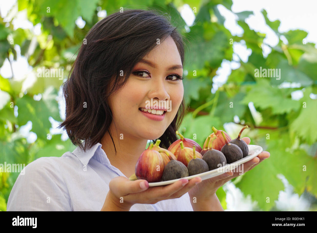 Young beautiful asian woman smile while holding a plate of fresh fig fruits. A good concept picture for fruit eating promoting healthy food and eating Stock Photo
