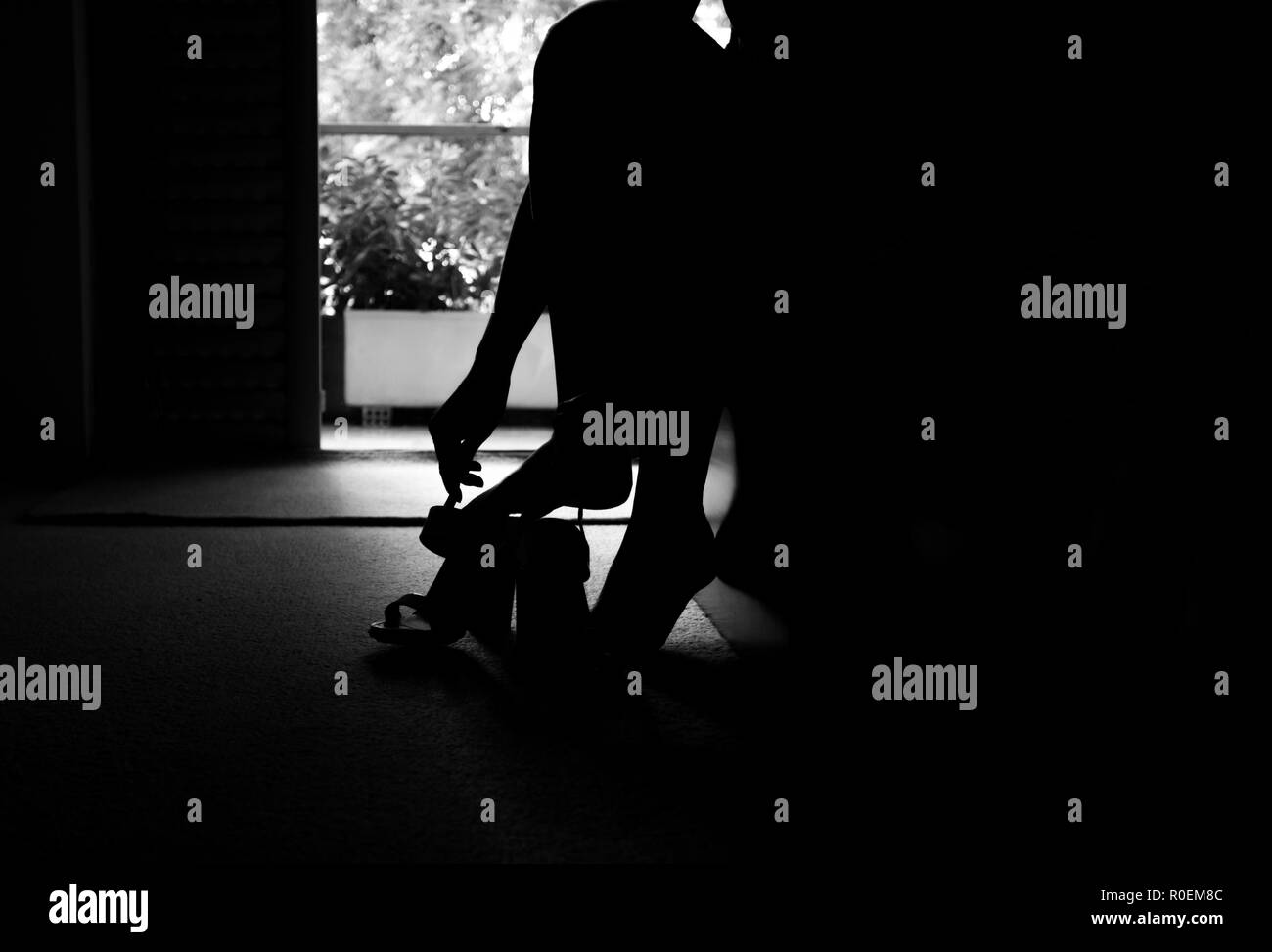 silhouette of a bride puts on wedding shoes on her feet background black and white Stock Photo