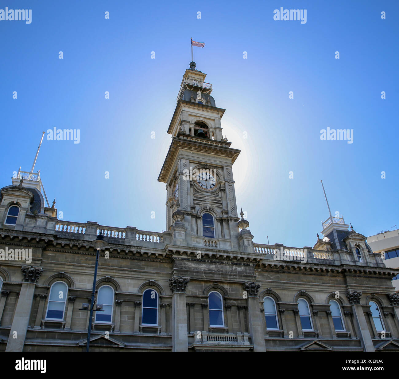 The clock tower on an old stone building in the city of Dunedin is lit up in the sunlight Stock Photo