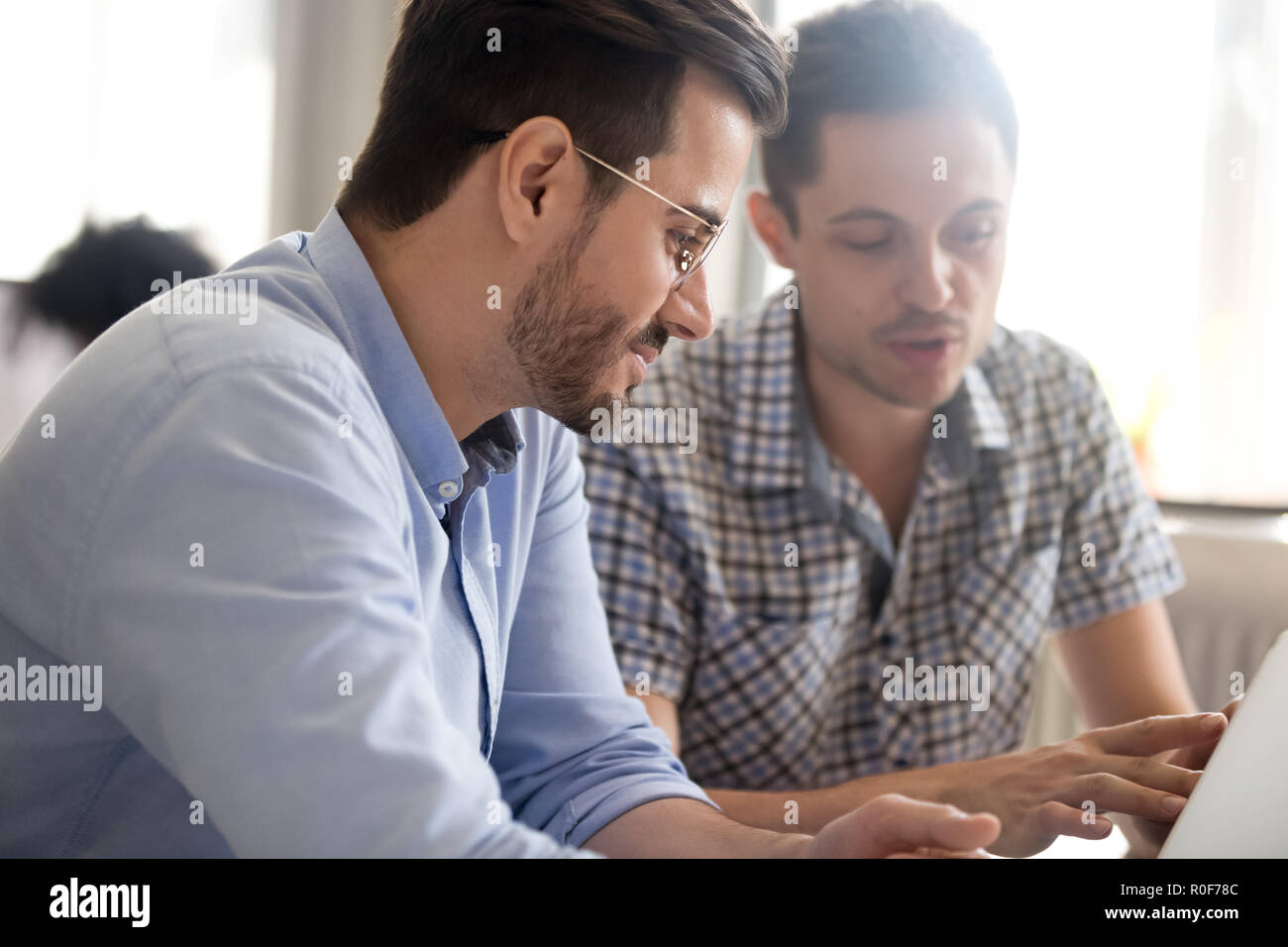 Focused male colleagues work together using laptop discussing on Stock Photo