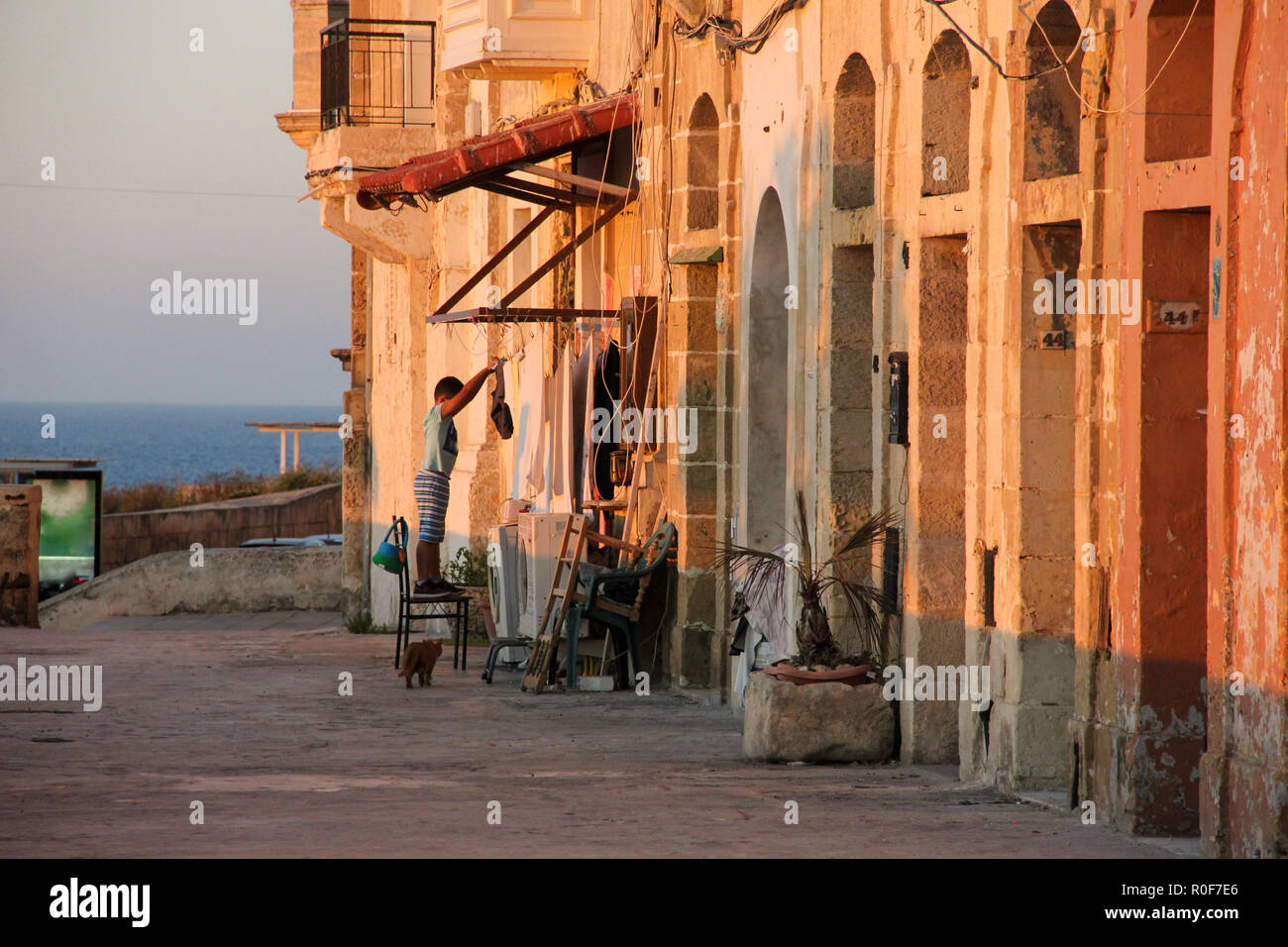 Valletta, Malta - May 2018: Real life on Malta see side during orange sunset - boy hanging clothes drying, two washing machines and gignger cat on the Stock Photo