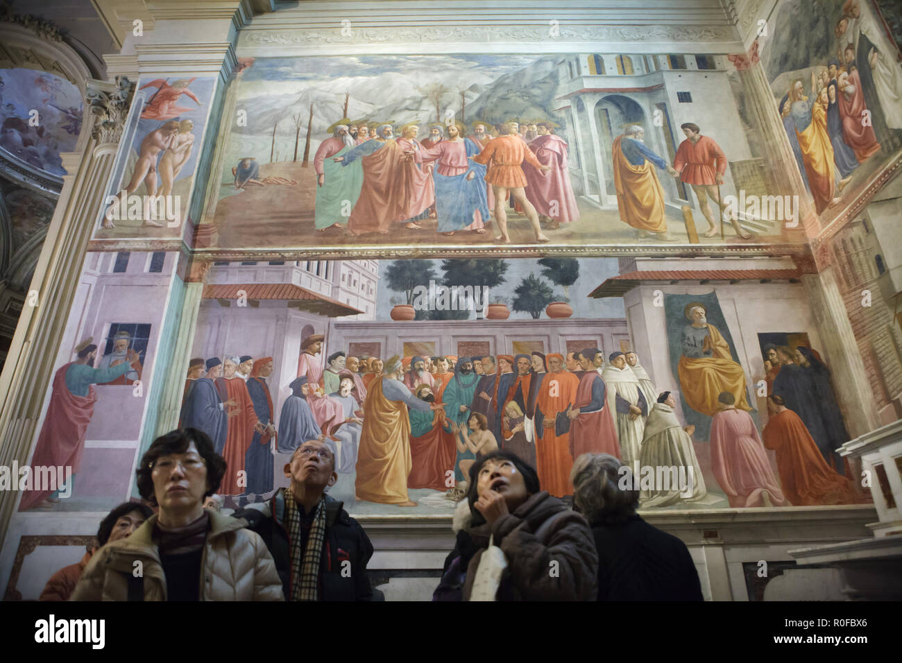 Asian visitors attend a guided tour in the Brancacci Chapel (Cappella Brancacci) in the Church of Santa Maria del Carmine in Florence, Tuscany, Italy. Frescos by Italian Renaissance painter Masaccio (1420-1427) completed by Filippino Lippi (1485) are seen in the background. Stock Photo