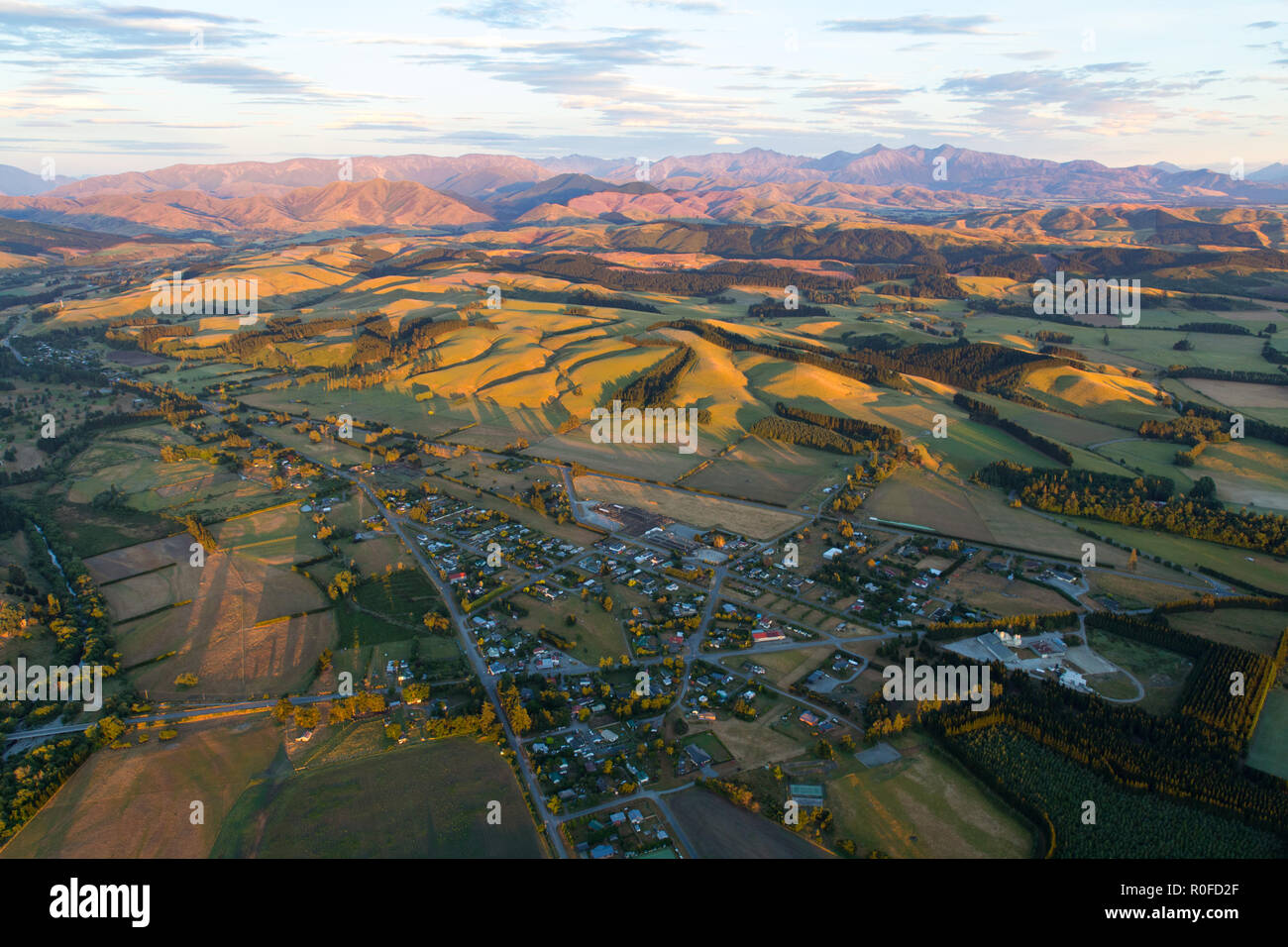The view from above in a hot air balloon of a town, surrounding hills, mountains, and the farm fields below in the early morning light Stock Photo