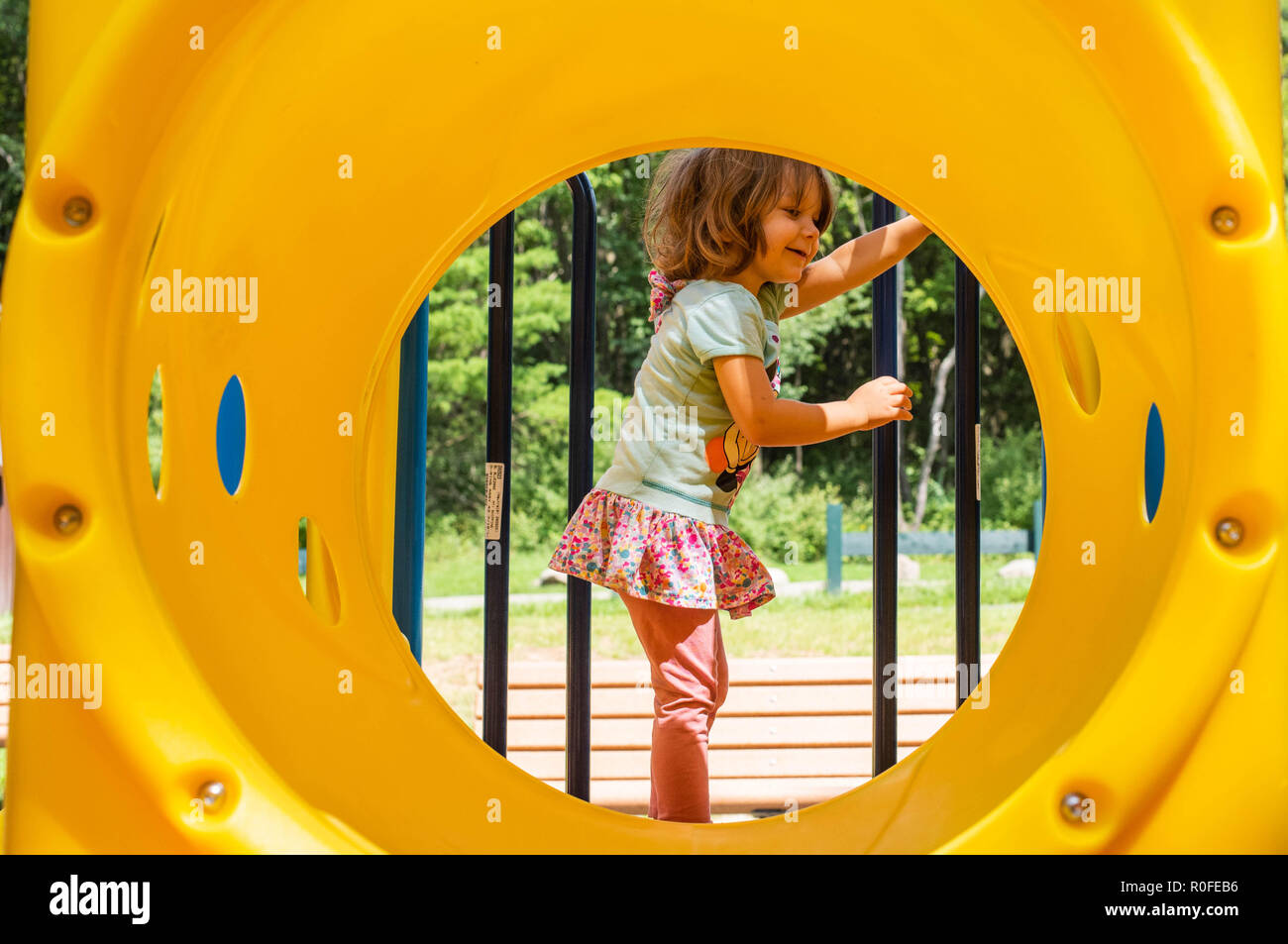 A 4-year old girl plays on playground equipment on a sunny summer day. Stock Photo