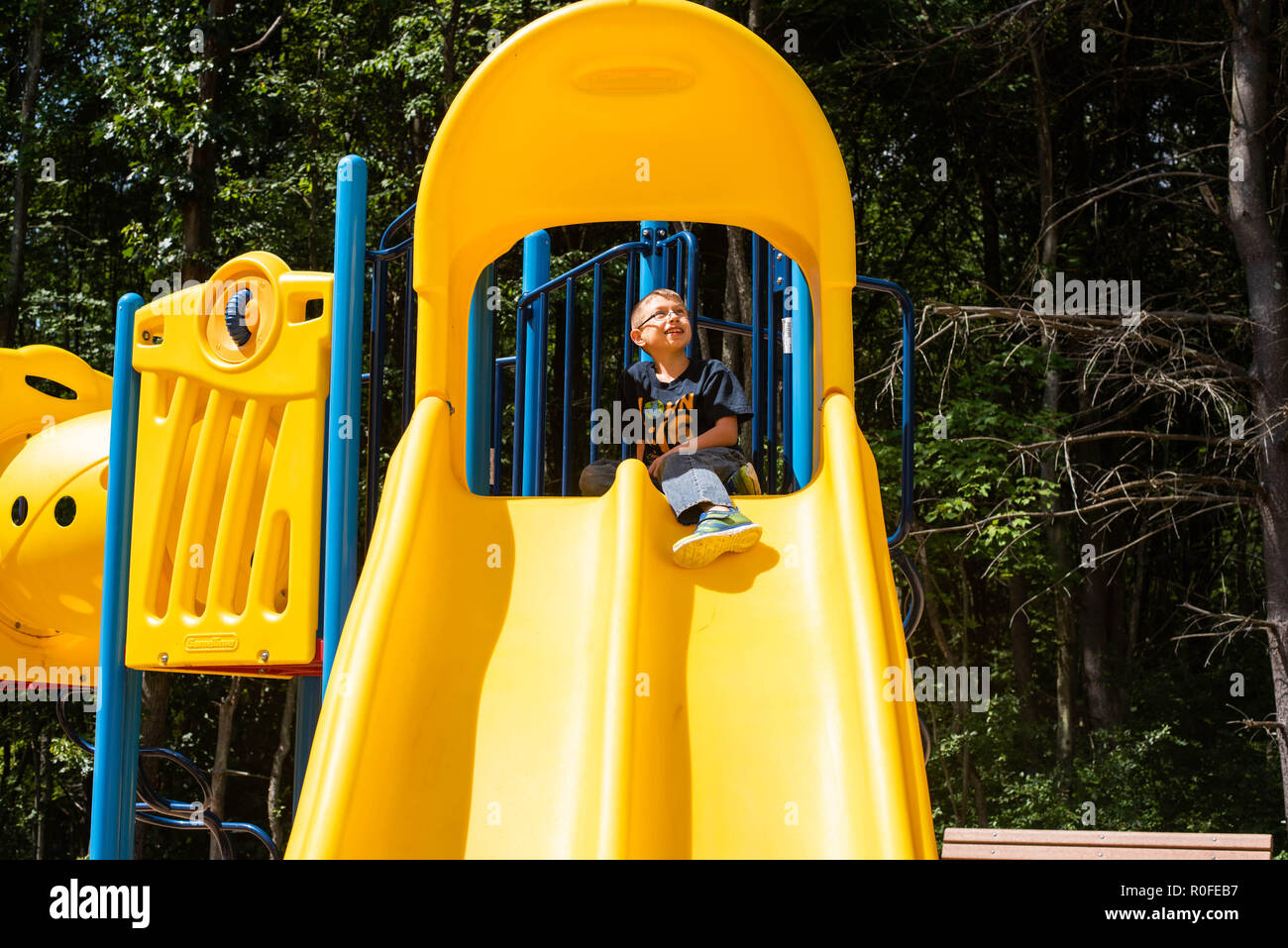 A 12-year old boy sits at the top of a yellow slide on a warm, sunny, summer day. Stock Photo