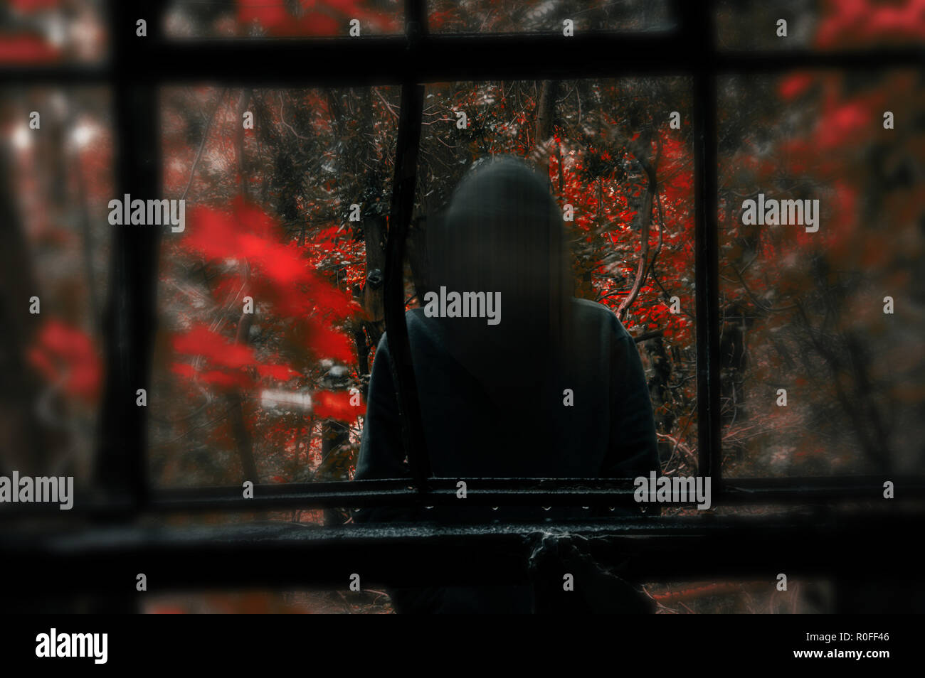 A sinister hooded figure with a blurred face looking into a ruined window frame. With a strong contrast and blurred Photoshop edit Stock Photo
