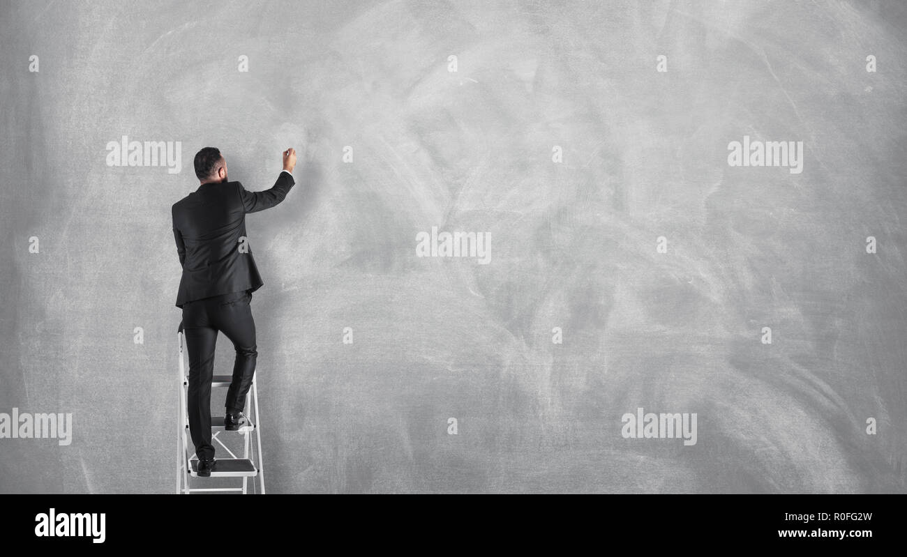 Businessman drawing on a blank concrete wall, announcement concept. Stock Photo