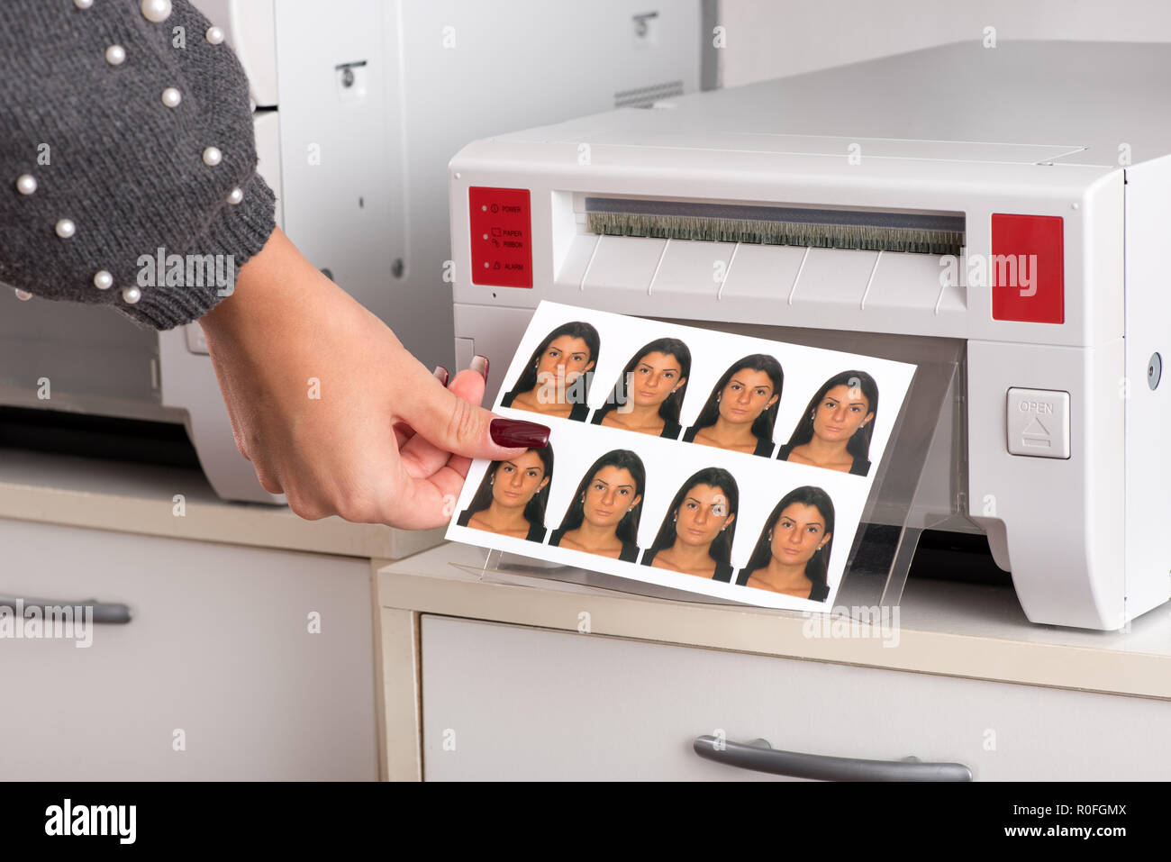 Set of just printed passport photos of a young woman exiting the printer with the hand of a woman reaching for the sheet in a close up view Stock Photo