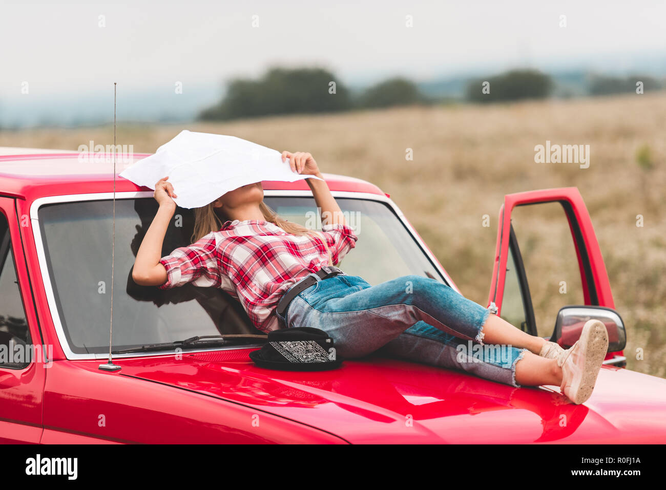 young woman lying on hood of vintage red truck in field and covering