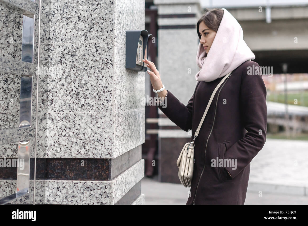 brunette woman calls into the intercom on the street, autumn day in warm clothes Stock Photo