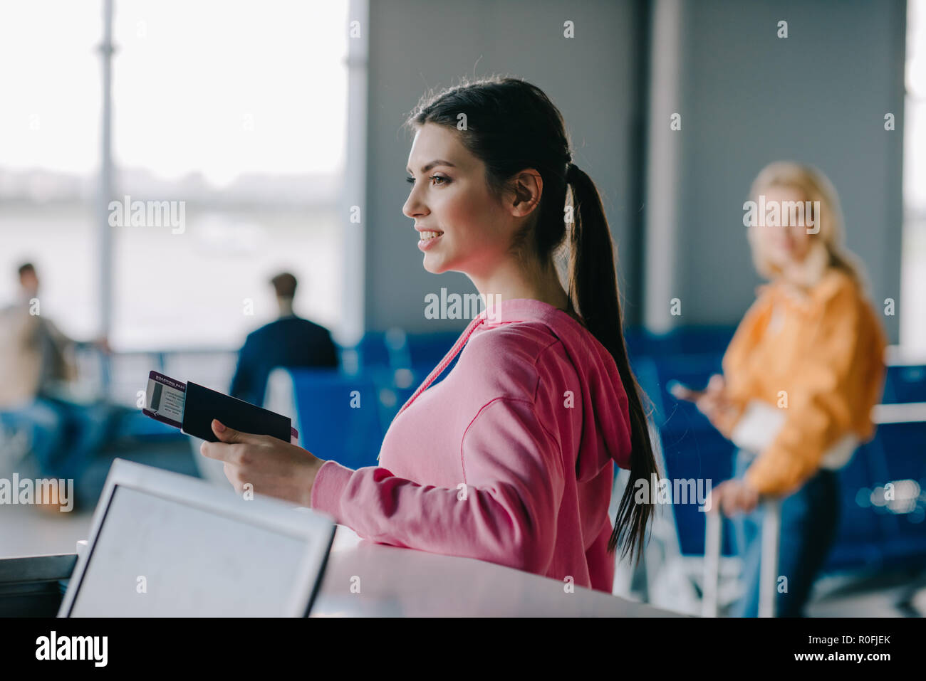 smiling young woman holding passport and boarding pass in airport terminal Stock Photo