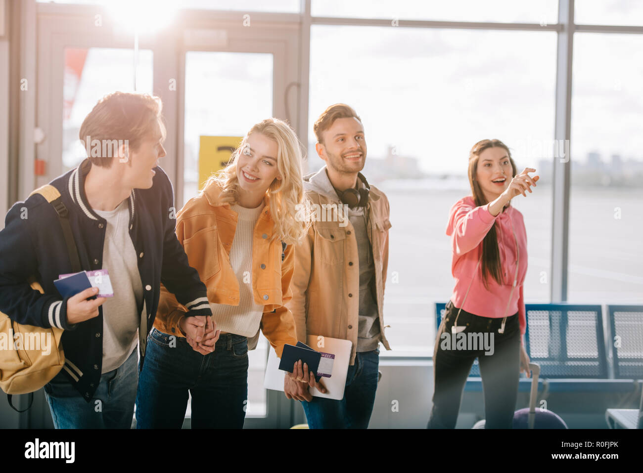 smiling young friends holding passports, boarding passes and luggage in