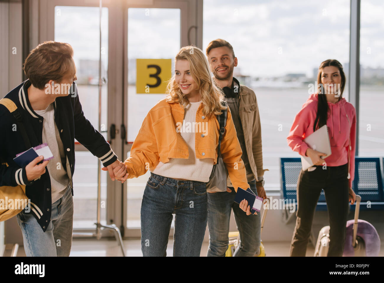 happy young friends holding passports, boarding passes and luggage in