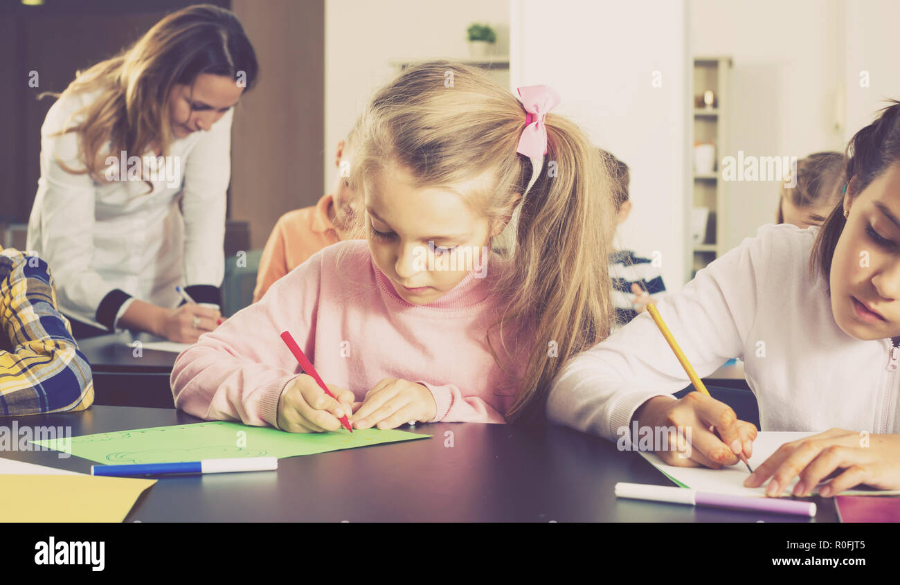 Portrait of girl and children in elementary age drawing at lesson in ...