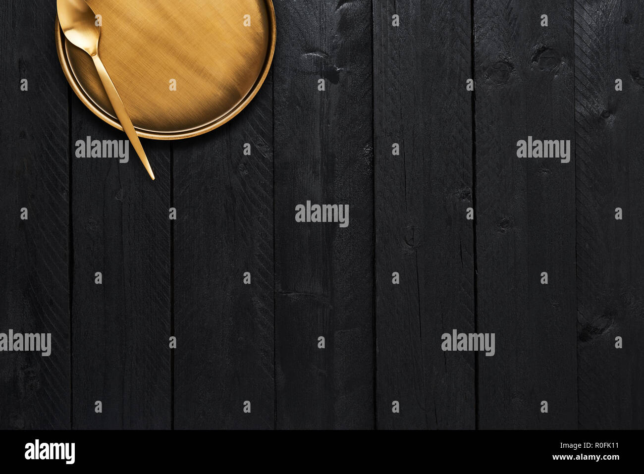 Top view of golden spoon and serving plate on black wooden table with copy space. Stock Photo