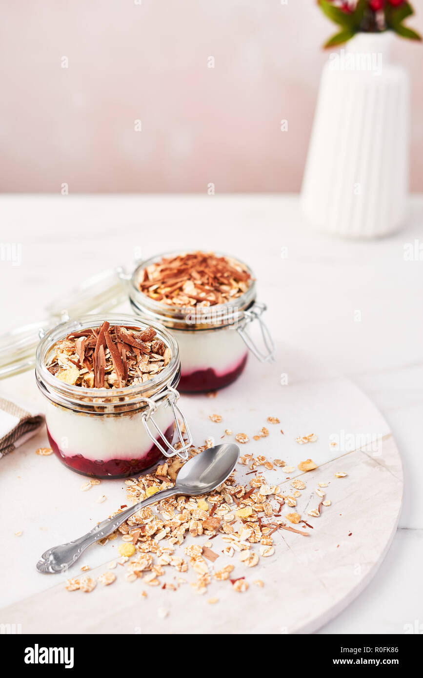 Healthy breakfast. Two jars of healthy yogurt with strawberry sauce, oat and chocolate on white marble serving plate over pink background with copy sp Stock Photo