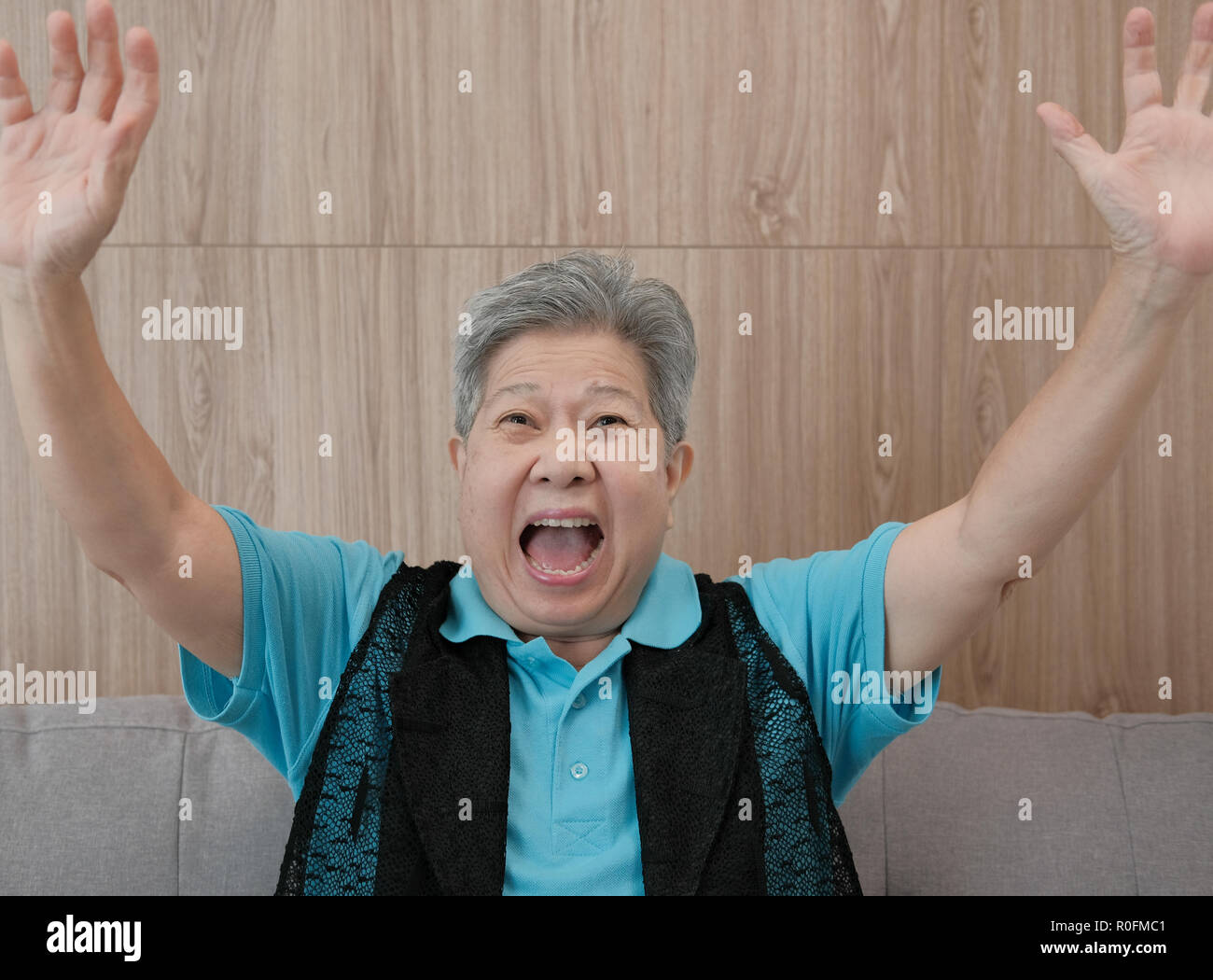 old asian elderly woman smiling & raising hands with gladness. happy elder senior sit on sofa at home Stock Photo