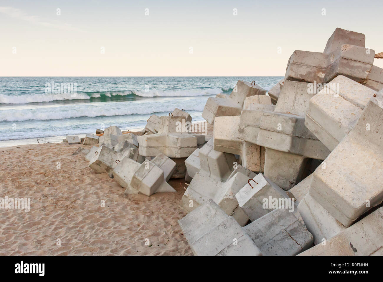 Breakwater with concrete blocks on sand beach, sunset Stock Photo