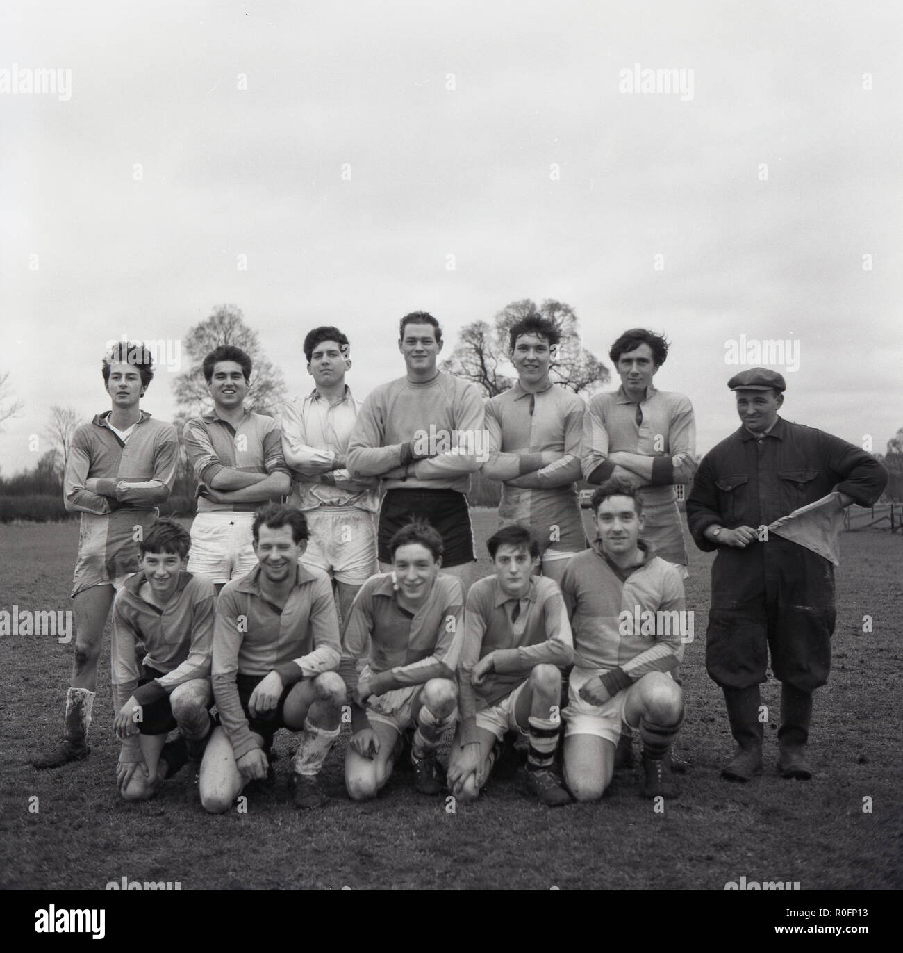 1964, group picture of the village football team in kit outside on the muddy pitch, with their mamager/linesman, Great Kimble, Buckinghamshire, England, UK. Stock Photo