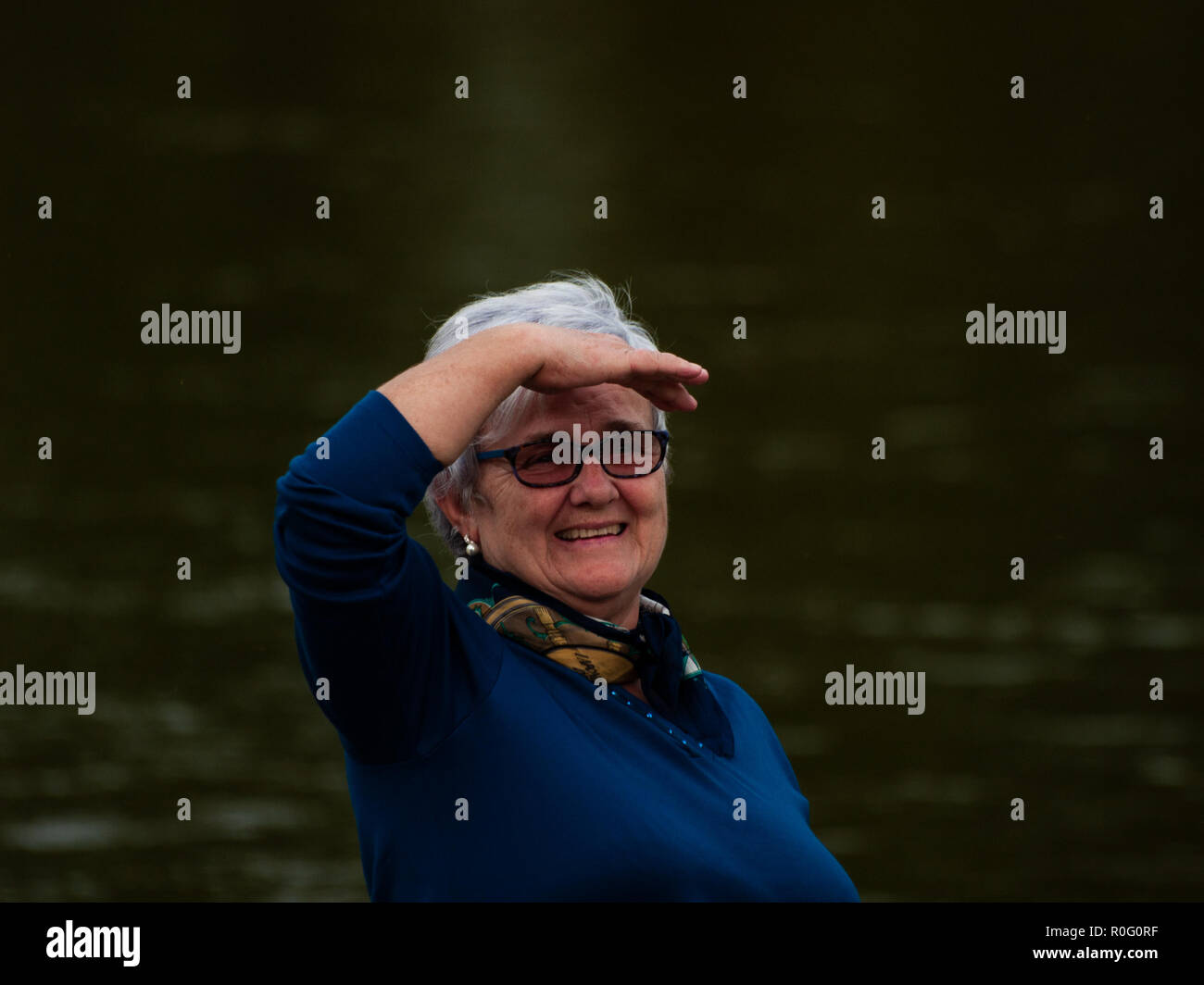 Una mujer mayor gesticulando y sonriendo a la orilla del río Stock Photo