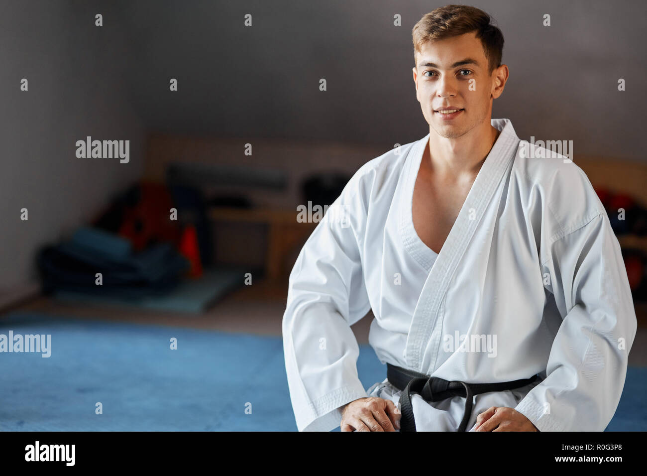 Karate man in kimono sits on knees on floor in martial arts gym Stock