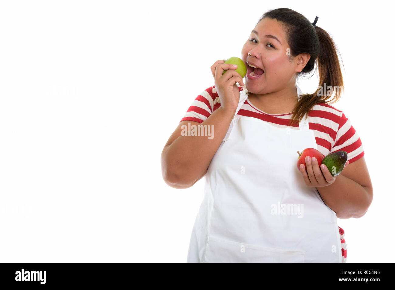 Studio shot of young happy fat Asian woman smiling and eating gr Stock Photo