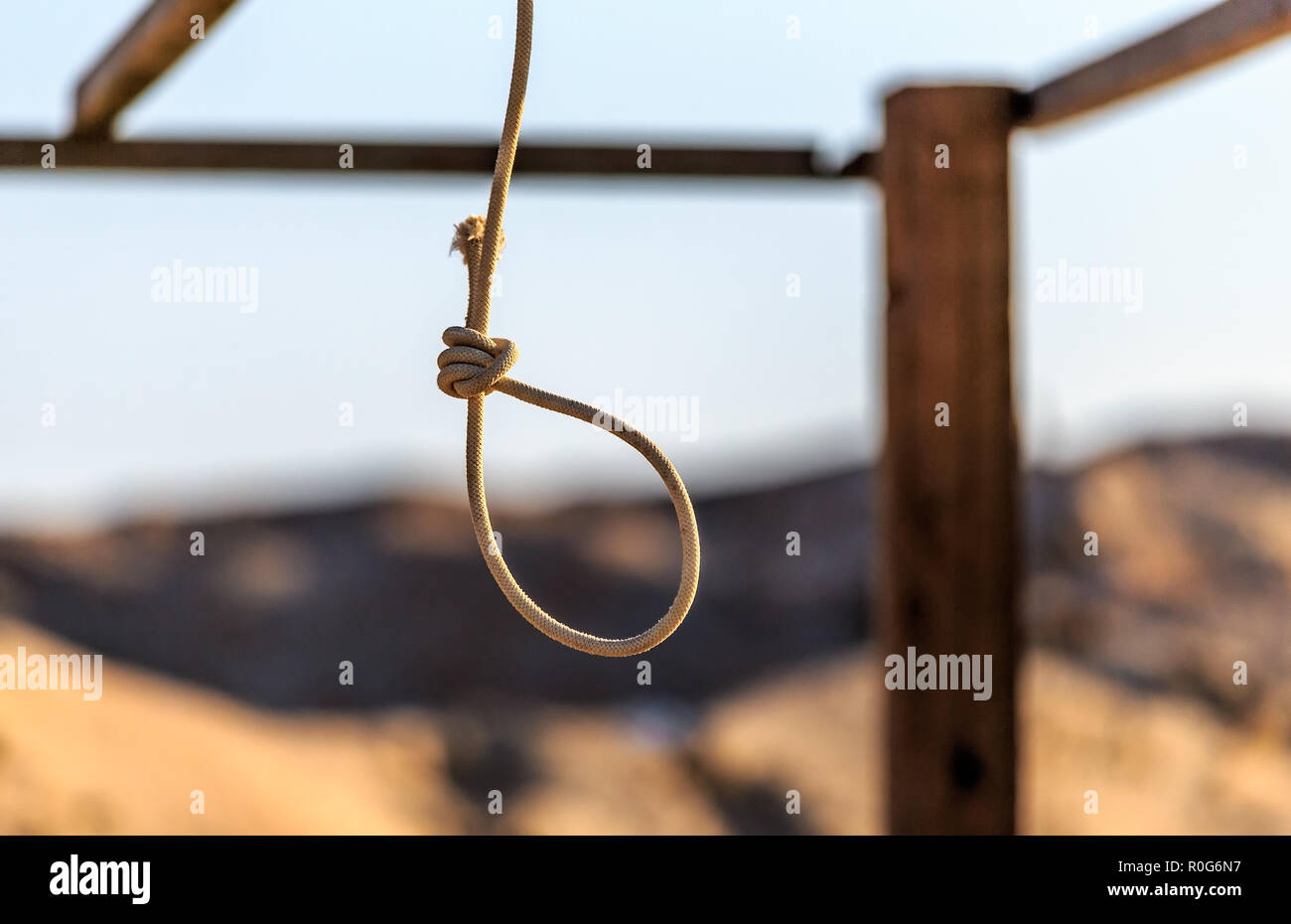 Rope noose hanging outdoors in sandy wilderness on sunny blue sky background. Scaffold for committing death punisment executions or suicide abstract i Stock Photo