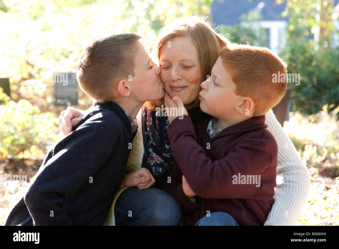 A red haired mother smiles peacefully as her two sons give her a gentle affectionate kiss Stock Photo