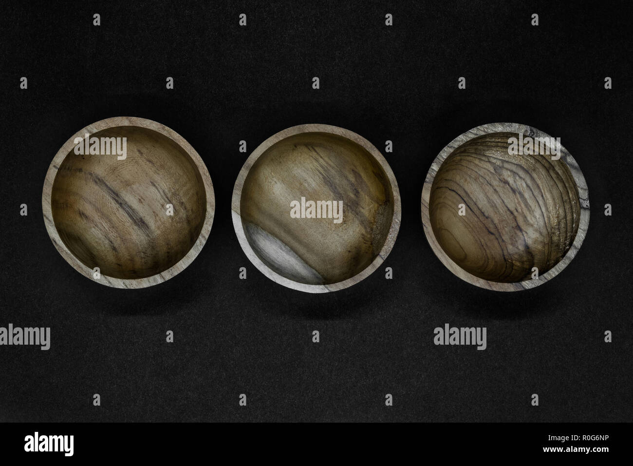 Three brown bowls made from palm tree wood placed in line on black