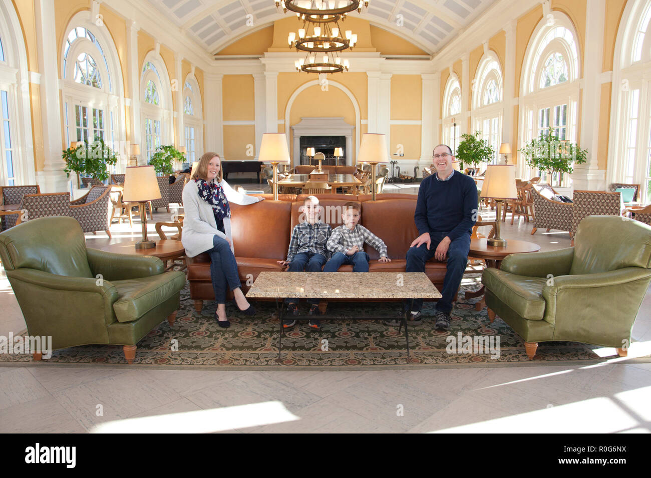 A family of four pose casually in a grand ballroom or recital space, lounging on the couch Stock Photo