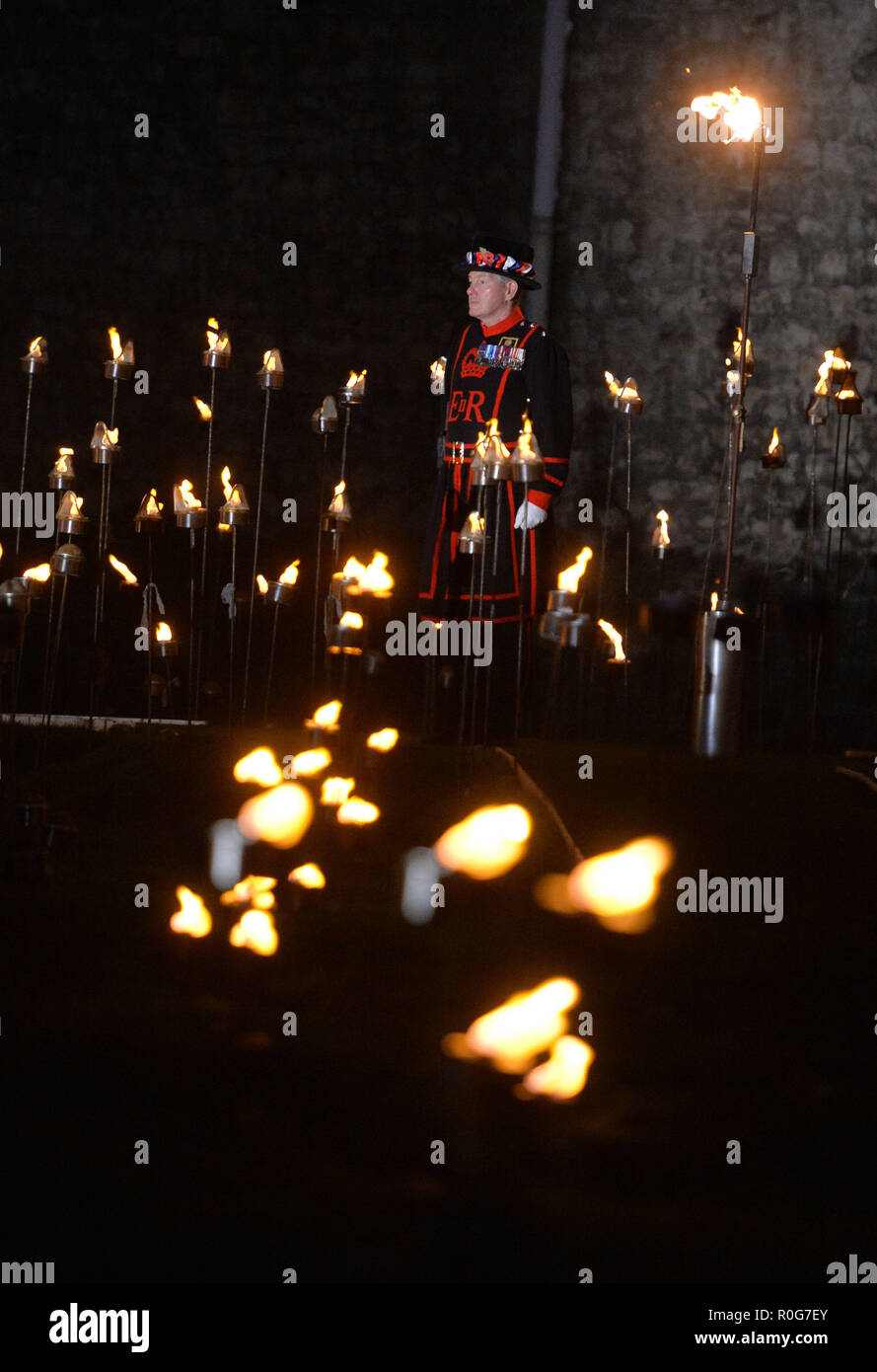 Yeoman Warders ('Beefeaters') lighting the first of thousands of flames in a lighting ceremony in the dry moat of the Tower of London as part of an installation called Beyond the Deepening Shadow: The Tower Remembers, to mark the centenary of the end of First World War. Stock Photo