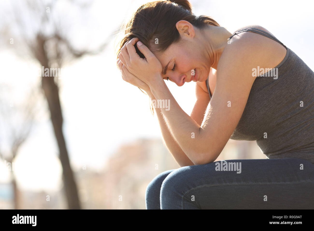 Profile of a sad teen crying desperately sitting on a bench in a park Stock Photo