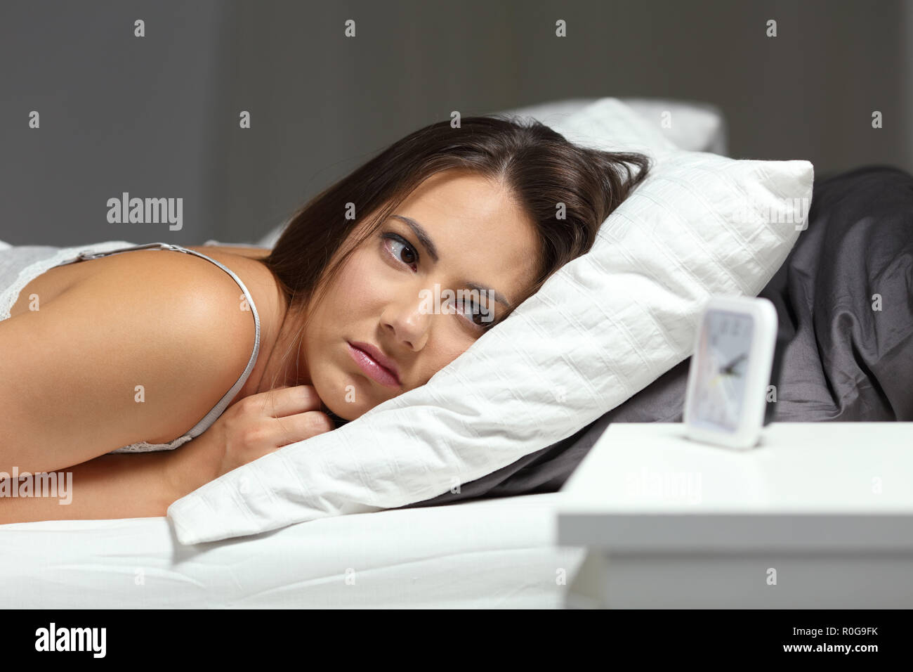 Sleepless insomniac girl looking at alarm clock lying on a bed in the night at home Stock Photo