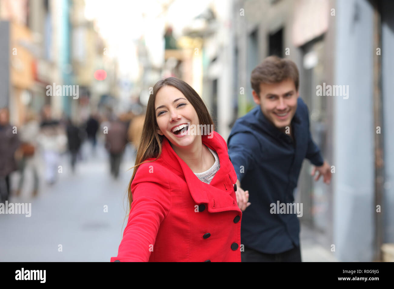 Happy couple running together towards camera in the street in winter Stock Photo