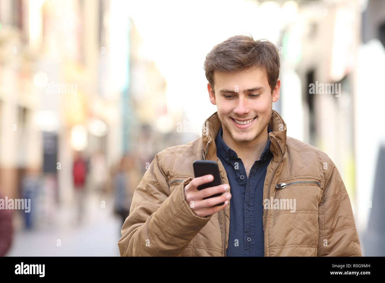 Front view of happy man texing on smart phone in winter in the street Stock Photo